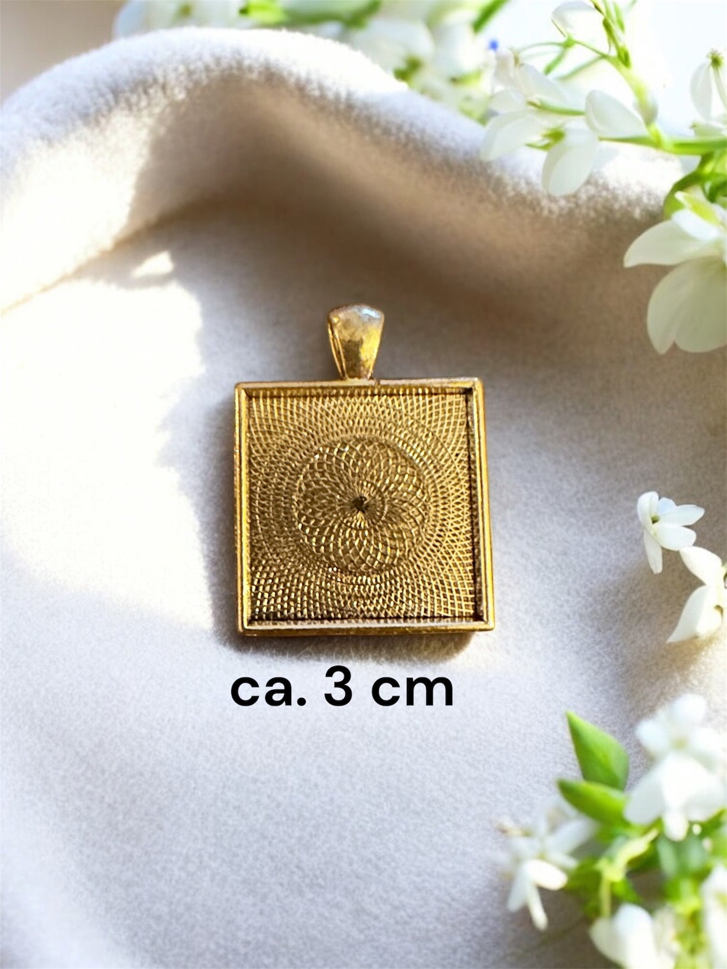 Größenvergleich eines quadratischen Gedenkschmuck Anhängers in Gold-Optik mit ca. 3 cm Seitenlänge.