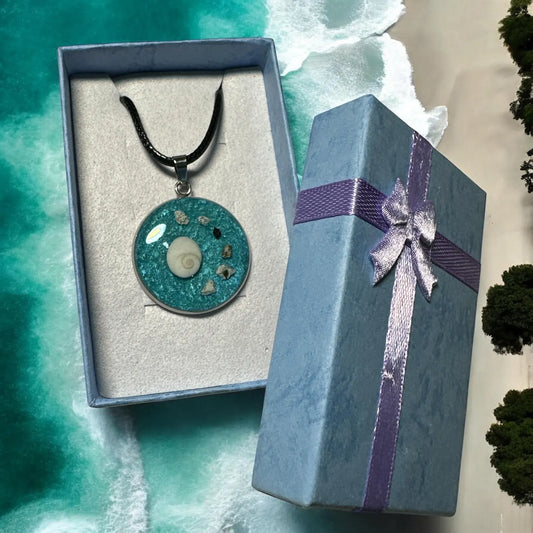 Runder Gedenkschmuck Anhänger aus Epoxidharz mit eingearbeiteter Asche neben einer blauen Geschenkbox mit silberner Schleife.
