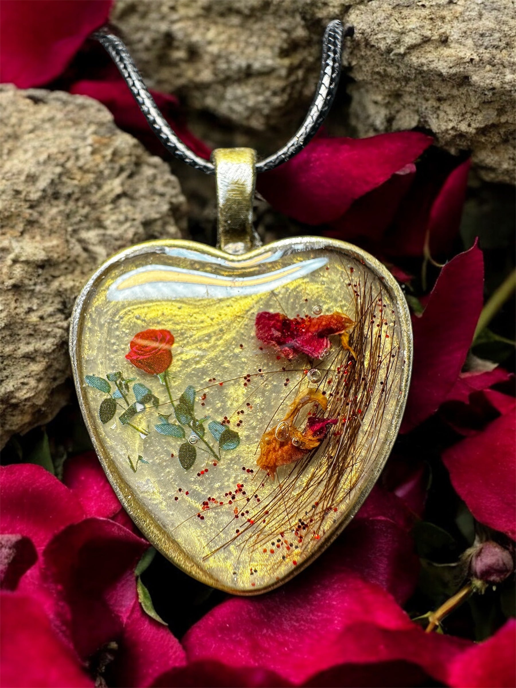 Gedenkschmuck Anhänger in Herzform mit eingearbeiteter Tierhaarsträhne und roten Blütenblättern auf dunklem Grund.