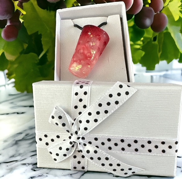 Kettenanhänger in Dubbeglas-Form mit rosa-orangefarbenem Farbverlauf, präsentiert in einer weißen Geschenkbox vor einer Weinberg-Kulisse.