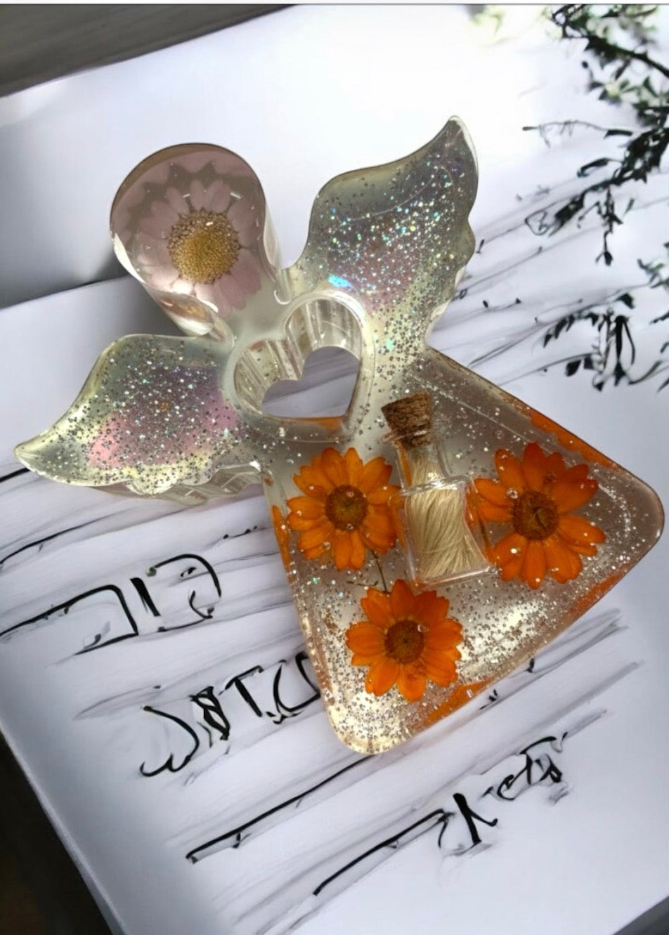 Gedenk-Engel aus klarem Epoxidharz mit eingearbeiteten orangefarbenen Trockenblumen, einer kleinen Glasphiole für Tierhaar und silbernen Glitzer-Akzenten