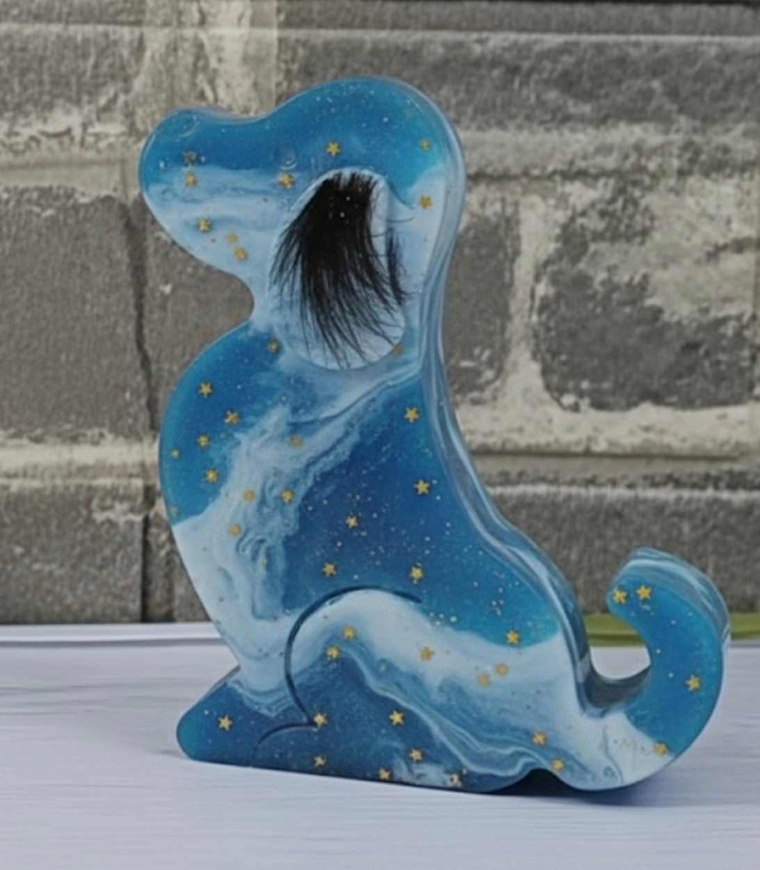 Blaue Gedenk-Figur in Hundeform aus Epoxidharz mit Marmorierung, kleinen goldenen Sternen und einer eingearbeiteten dunklen Tierhaar-Locke.