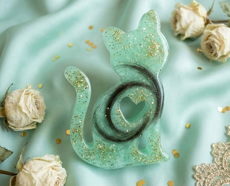 Mintgrüne Katzen-Erinnerungsfigur aus Epoxidharz mit Glitzereffekten und einer kunstvoll eingearbeiteten dunklen Felllocke.“