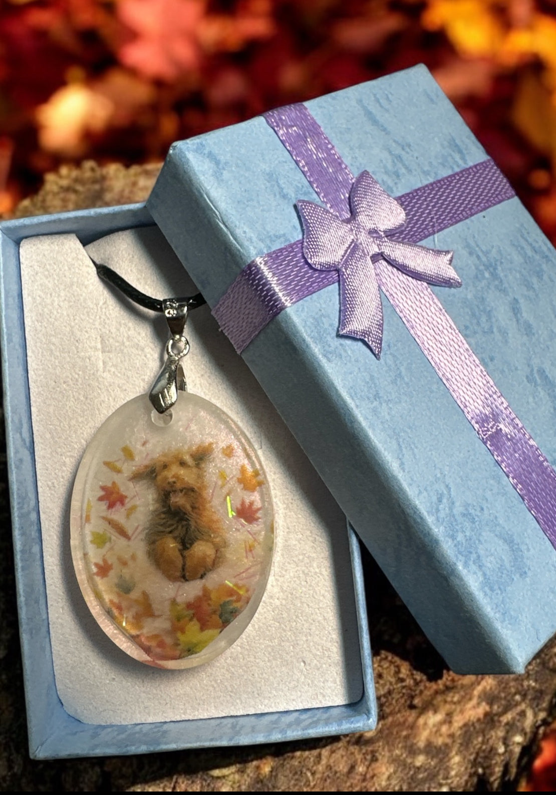 Personalisierter Schmuckanhänger mit Tierhaar-Andenken und kleinen Blumen-Akzenten in einer hellblauen Geschenkbox.