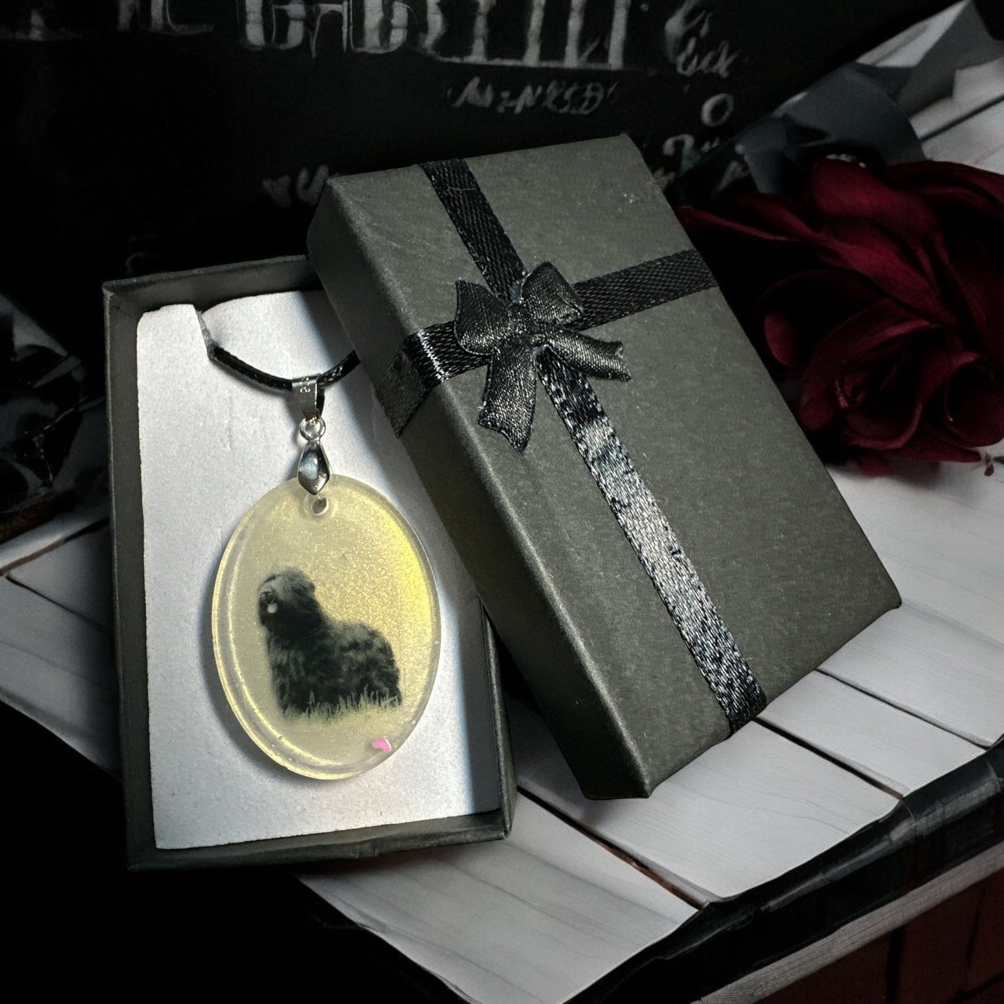 Ovaler Gedenkschmuck-Anhänger aus Epoxidharz mit der Silhouette eines Hundes "Phoenix"und eingearbeiteten Tierhaaren neben einer eleganten Geschenkbox.