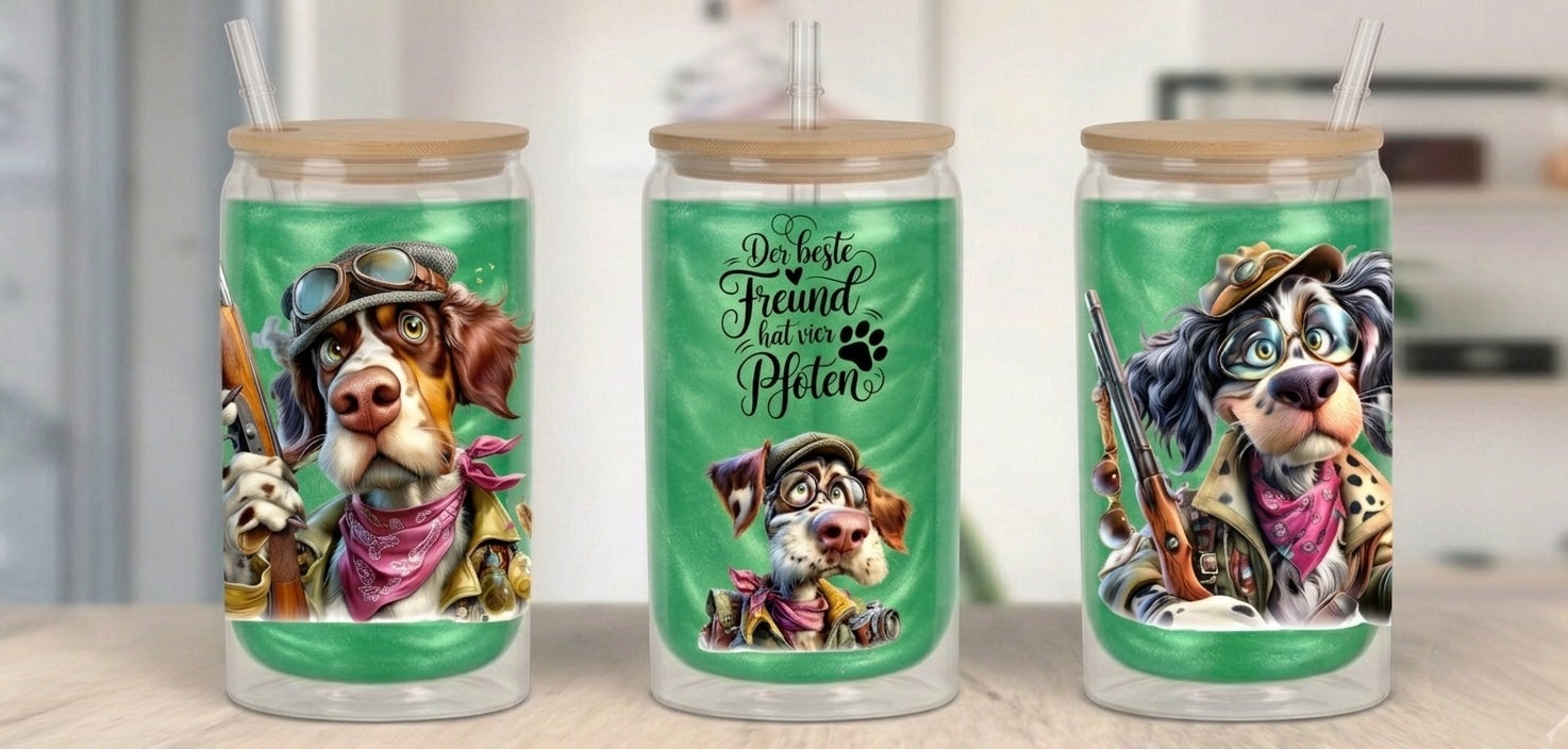Drei Trinkbecher mit Holzdeckeln und Strohhalmen, gefüllt mit einem glitzernden grünen Getränk. Die Becher zeigen humorvolle Illustrationen von Jagdhunden im Vintage-Stil: Links ein Hund mit Fliegerbrille und Jagdgewehr, mittig der Schriftzug „Der beste Freund hat vier Pfoten“ über einem kleineren Hundekopf und rechts ein bebrillter Hund mit Hut und Gewehr.