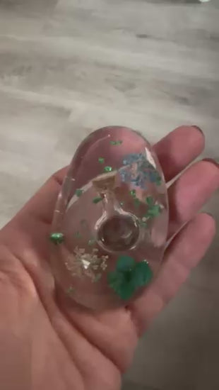 Video-Demonstration eines handgefertigten Handschmeichlers aus klarem Epoxidharz, der im Licht gedreht wird, um die eingearbeiteten blauen und grünen Blüten sowie die Glitzereffekte detailreich zu zeigen