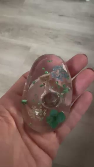 Video-Demonstration eines handgefertigten Handschmeichlers aus klarem Epoxidharz, der im Licht gedreht wird, um die eingearbeiteten blauen und grünen Blüten sowie die Glitzereffekte detailreich zu zeigen
