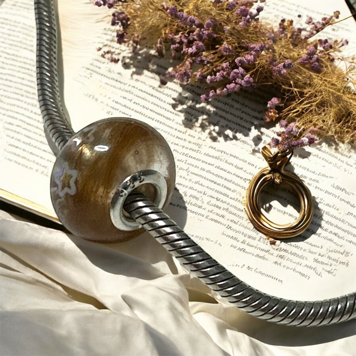 Handgefertigter Glas-Charm mit eingearbeiteten Tierhaaren auf einer silbernen Schlangenkette, präsentiert auf einem antiken Notenblatt mit getrocknetem Lavendel.